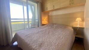 Habitación de hotel con una cama grande, una mesita de noche con lámpara, un armario de madera y una puerta corrediza de vidrio que da a un balcón.