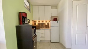 Una cocina compacta con muebles blancos, un horno negro y un refrigerador blanco.