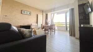 Una sala de estar con sofá, una mesa de comedor con sillas, televisor y un balcón con vistas.