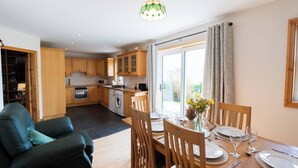 A modern kitchen with wooden cabinets, a dining area with a table set for four, and a large window with curtains.