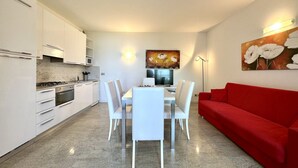 Une cuisine moderne avec des meubles blancs, une table à manger avec des chaises, un canapé rouge et des œuvres d’art accrochées aux murs.