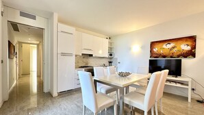 Une cuisine moderne avec des meubles blancs, une table à manger entourée de chaises blanches et un tableau accroché au mur.