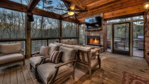 A wooden deck with a stone fireplace, leather sofas, and a flat-screen TV. - Jazzy's Cozy Creekside - Hot Tub | Game Room | Screened Decks (Blue Ridge)