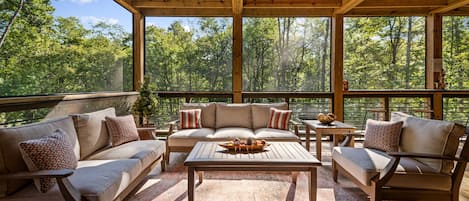 An outdoor seating area with a wooden ceiling, a ceiling fan, and a view of a forest.