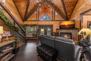L’intérieur d’une cabane en rondins, avec une cheminée, un canapé, un escalier et un livre d’or posé sur une étagère.