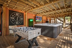 Een ruimte met houten vloer, voorzien van een tafelvoetbaltafel, een grote wandklok en een televisietoestel dat een sportwedstrijd toont.