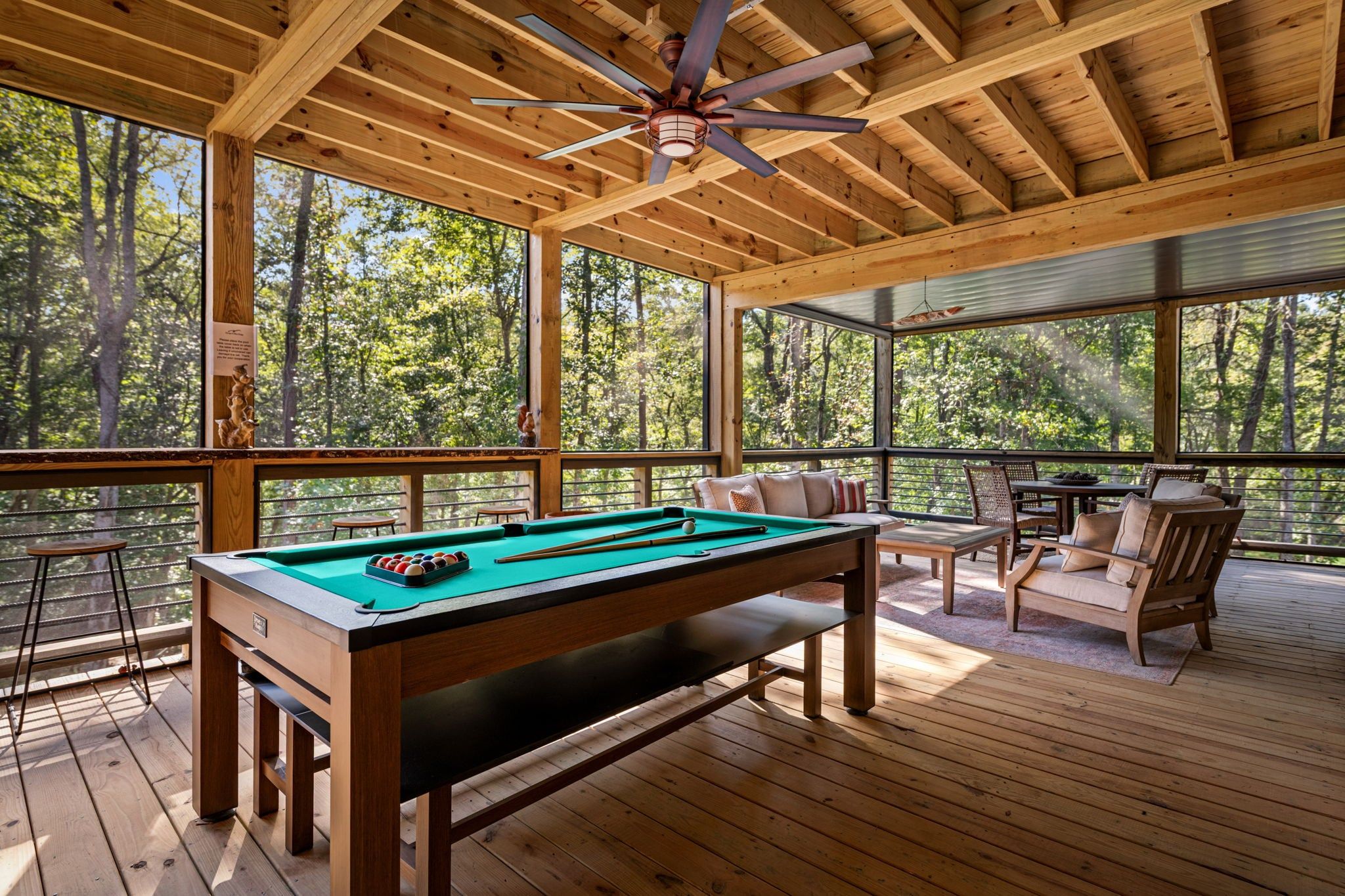 A wooden deck with a pool table, chairs, and a ceiling fan.