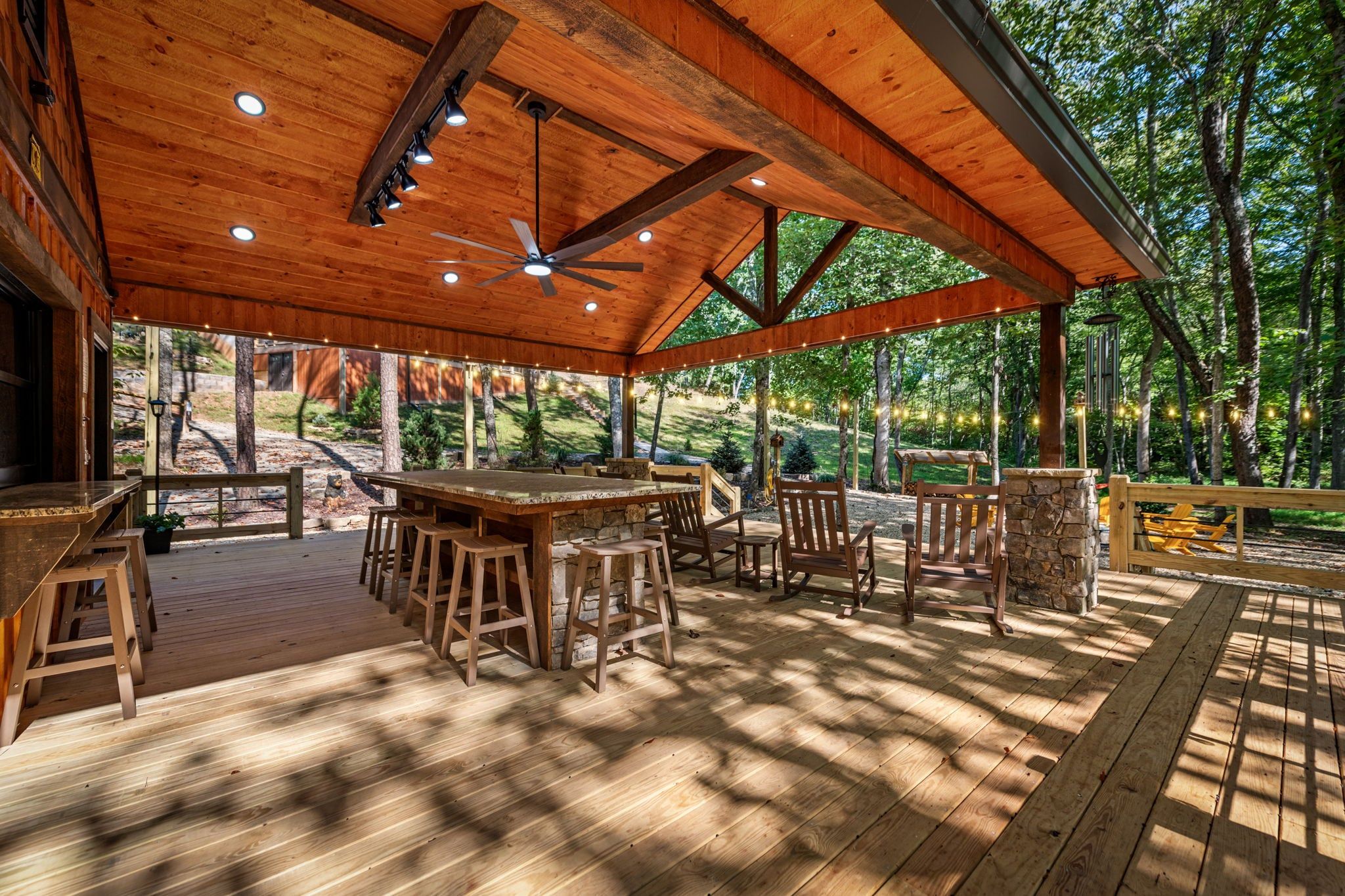 An outdoor wooden deck with a dining area, including a table and chairs, and a ceiling fan.