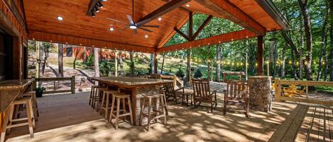 An outdoor wooden deck with a dining area, including a table and chairs, and a ceiling fan.