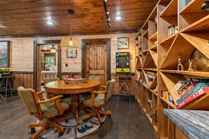 Ein Holzinterieur mit einem runden Esstisch, Stühlen, einer Hängelampe und einem Bücherregal mit Gesellschaftsspielen.
