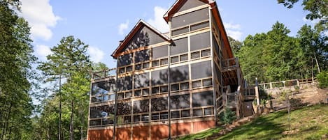A modern multi-story building with large windows, a sloped roof, and a wooden staircase leading up to it.