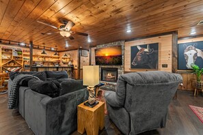 A cozy living room with a fireplace, wooden ceiling, and a bookshelf filled with books and decorative items.