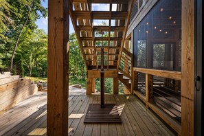 Una terraza de madera con una estructura de pérgola, rodeada de abundante vegetación.