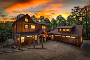 Une maison en bois à deux étages, avec un garage, entourée d’arbres.