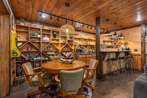 A wooden interior with a round dining table, chairs, and a kitchen area with bar stools.