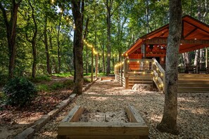 Une cabane en bois dotée d’une terrasse, entourée d’arbres et bordée de chemins de gravier.