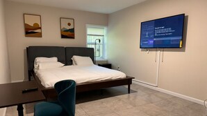 Ein Schlafzimmer mit einem Bett, einem Schreibtisch, einem Stuhl und einem an der Wand befestigten Fernseher.