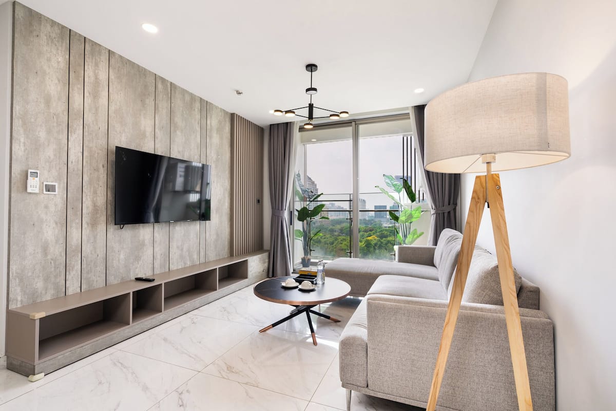Una sala de estar moderna con un televisor de pantalla plana montado en una pared de madera, una mesa redonda de centro con adornos, un sofá color beige y una lámpara de pie.