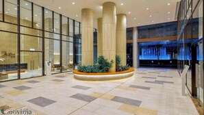 Un lobby espacioso con amplias ventanas de vidrio, una columna central con plantas y un diseño moderno.