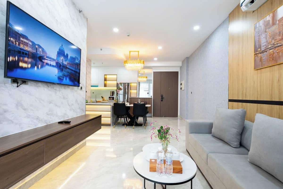 Un moderno vestíbulo de hotel con una gran televisión de pantalla plana, una recepción, un área de comedor y un espacio de descanso con un sofá y una mesa de centro.