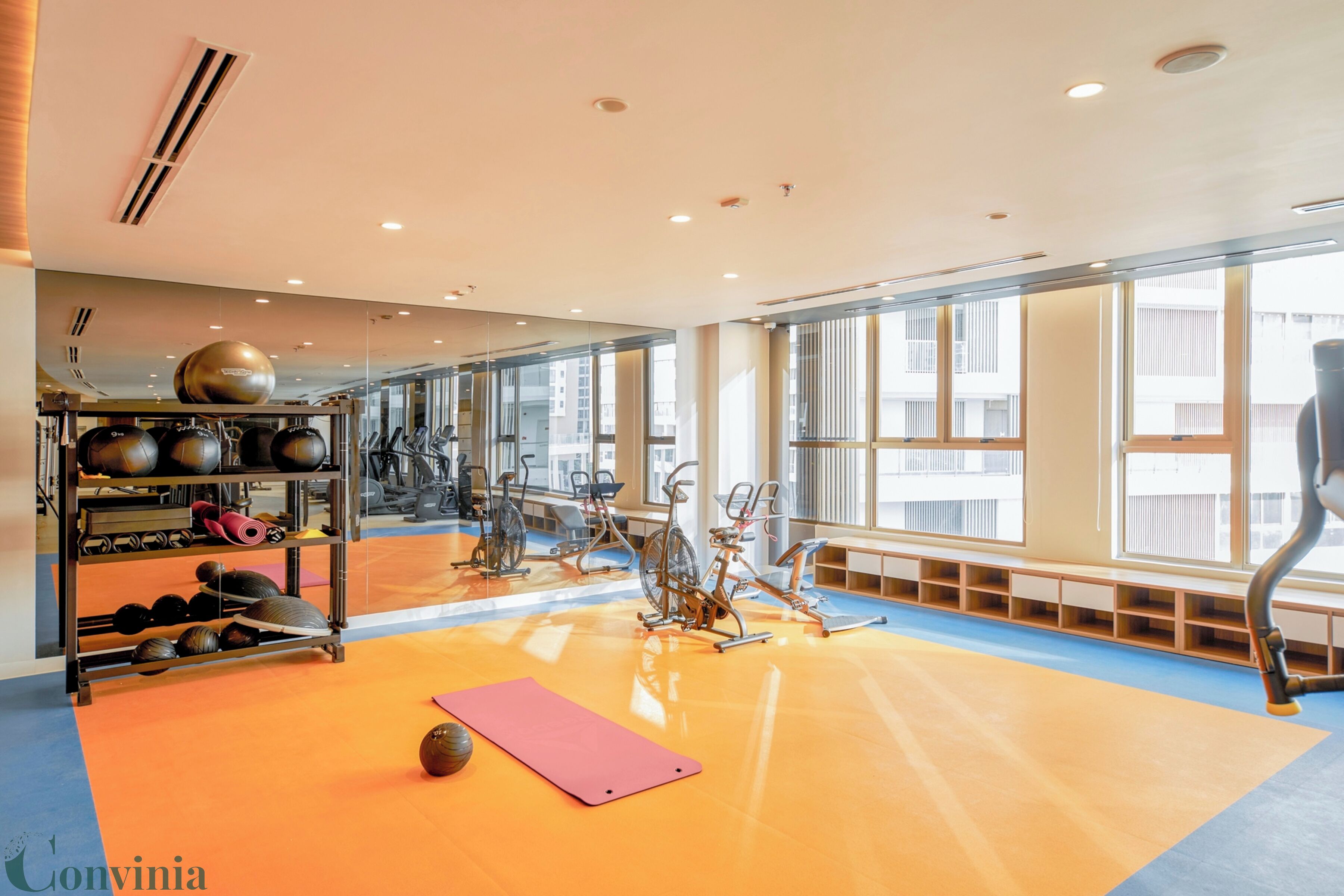 Academia com equipamentos de ginástica, tapete de yoga e um espelho.