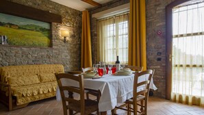 Un comedor con pared de piedra, un cuadro, un sofá y una mesa para dos, con copas de vino y una botella.