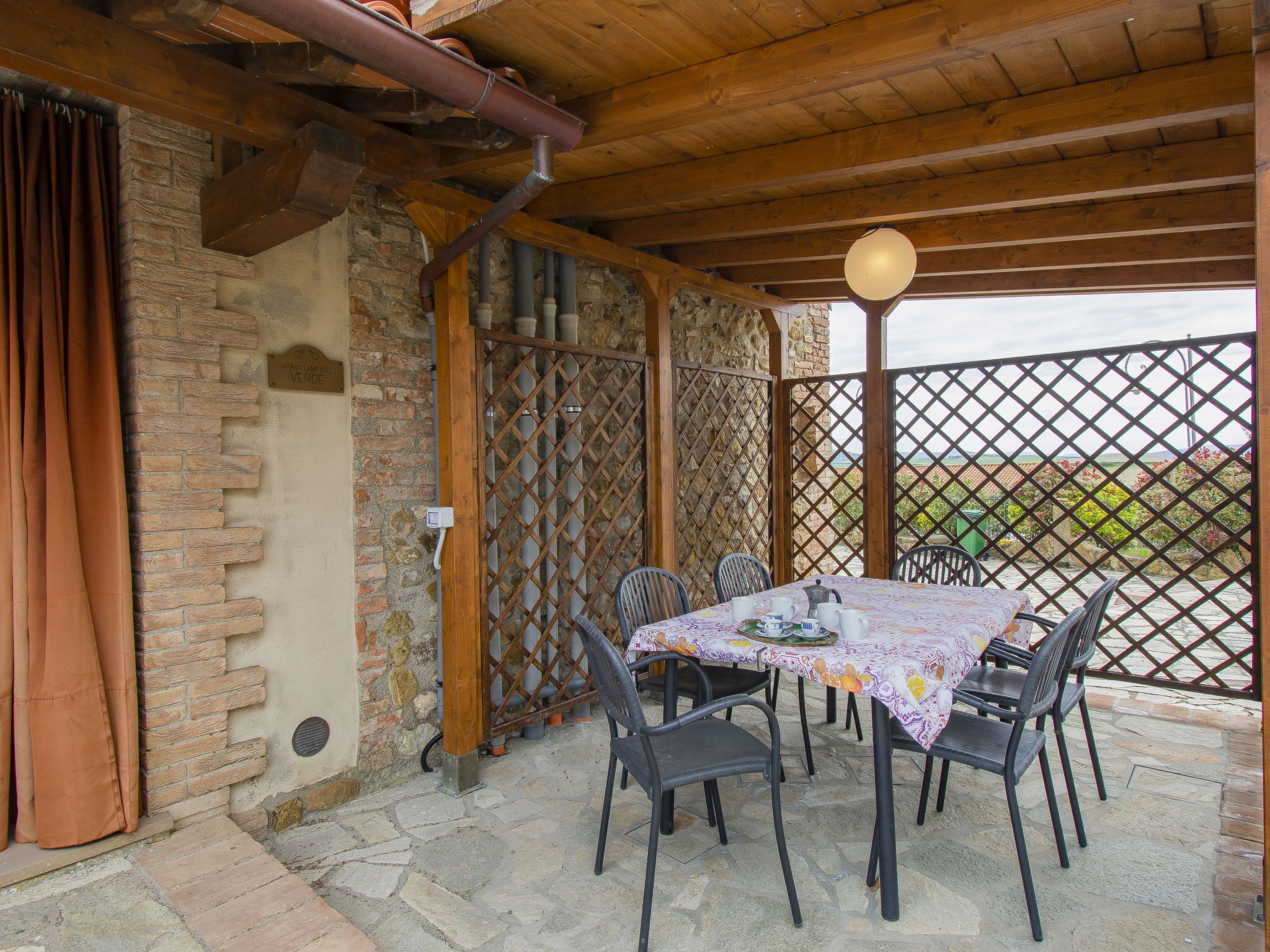 Un espace extérieur abrité, aménagé pour les repas, avec une table pour quatre personnes, entouré de murs en pierre et surmonté d’un plafond en bois.