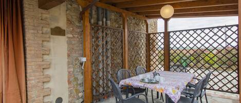 Un espace extérieur abrité, aménagé pour les repas, avec une table pour quatre personnes, entouré de murs en pierre et surmonté d’un plafond en bois.