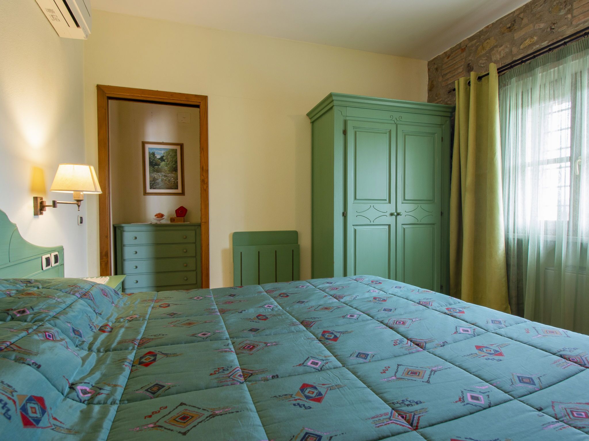 Ein Schlafzimmer mit Bett, Schminktisch, Kleiderschrank, Nachttisch, Lampe und einem Bild an der Wand.