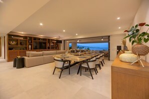 Uma sala de estar moderna com área de jantar, sofá, estante de madeira e vista para o mar.