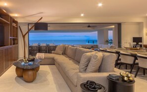 Uma sala de estar moderna com um amplo sofá de canto, uma área de jantar com balcão e vista para o oceano.