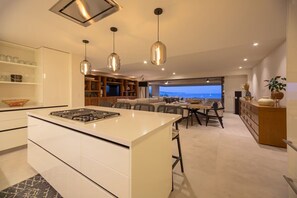 Cozinha moderna com ilha central, iluminação pendente e vista para o mar.