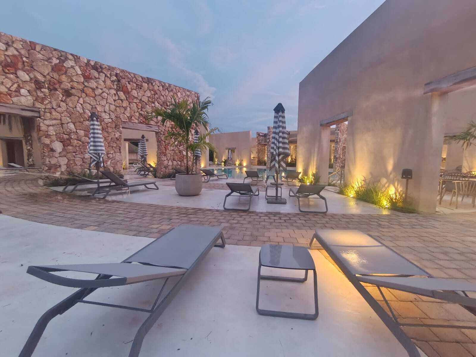 A courtyard with lounge chairs, a swimming pool, stone walls, and a modern building.