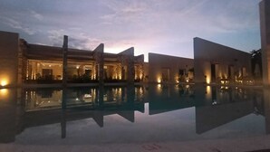 A pool with clear reflections, a building with stone pillars, and a sunset sky. - LJS Chichikan Eco Luxury Retreat  (Valladolid)