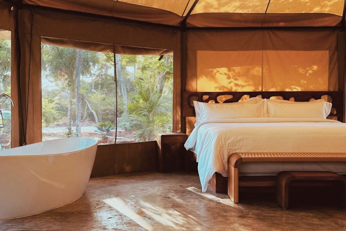 A tent-style bedroom with a large bed, a bathtub, and a view of the outdoors.