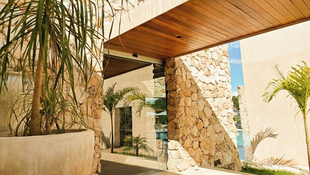 A modern architectural structure with a stone facade, a wooden ceiling, and a concrete pathway. - LJS Chichikan Eco Luxury Retreat  (Valladolid)