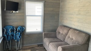 A room with a grey couch, a window with blinds, and two blue chairs.
