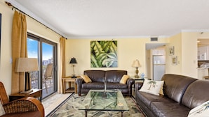 Ein Wohnzimmer mit Glastisch, Ledersofas, einem großen Fenster mit Vorhängen und Blick auf die Stadt.