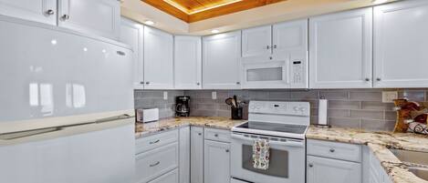 A modern kitchen with white cabinets, a stainless steel refrigerator, a microwave, and an oven.