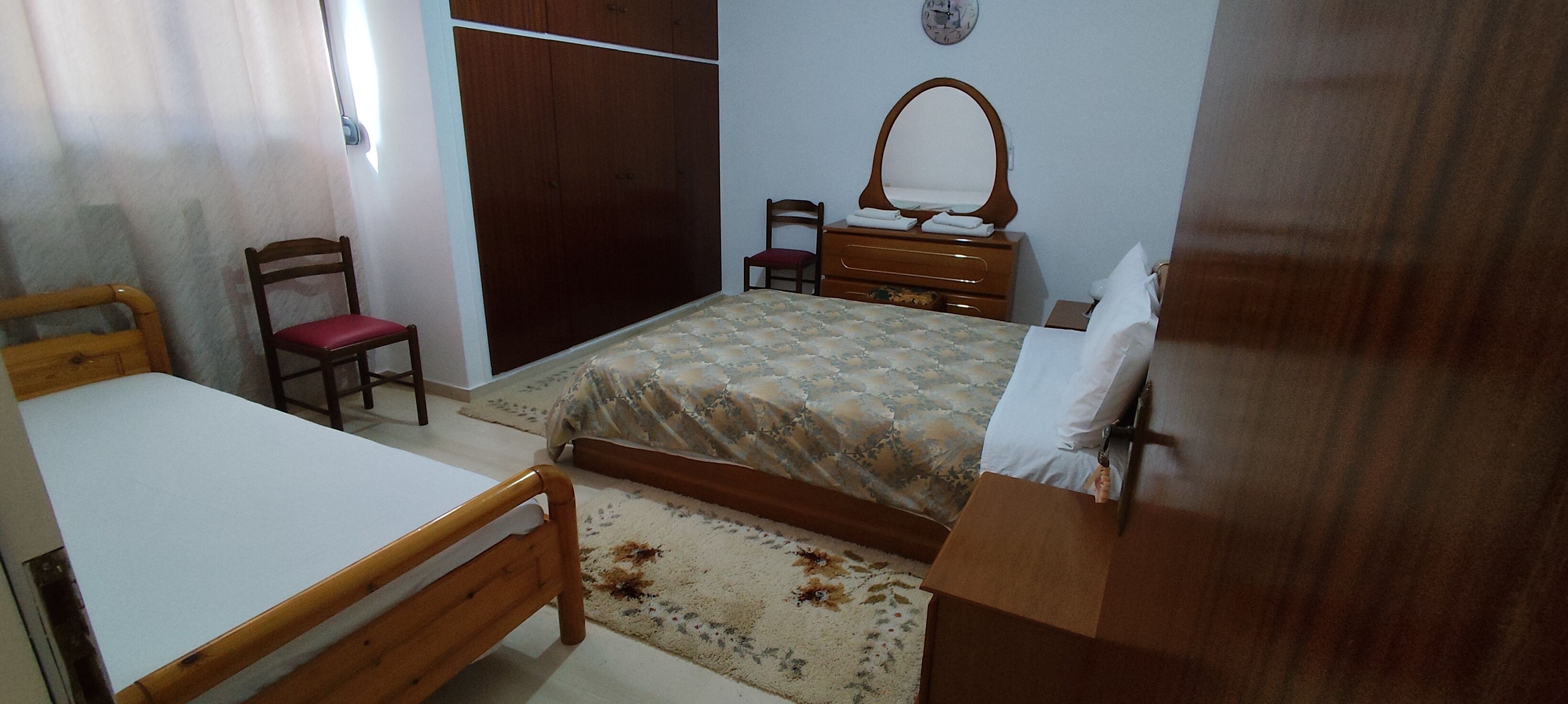 Un dormitorio con una cama, una silla de madera, un aparador y un armario.