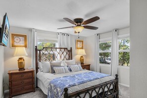 A bedroom with a four-poster bed, two bedside tables with lamps, a ceiling fan, and large windows with curtains. - Heated Pool, Outdoor Dining & Grill, Near the Beach - Heart of Punta Gorda - Roelens (Punta Gorda)