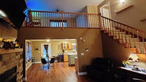A spacious living area with a fireplace, a dining table with chairs, a kitchen in the background, and a wooden staircase. - Romantic couples getaway in awesome Bluford with WiFi, Fireplace, and Game Room (Bluford)
