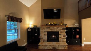A living room with a stone fireplace, a mounted TV, and a bookshelf. - Romantic couples getaway in awesome Bluford with WiFi, Fireplace, and Game Room (Bluford)