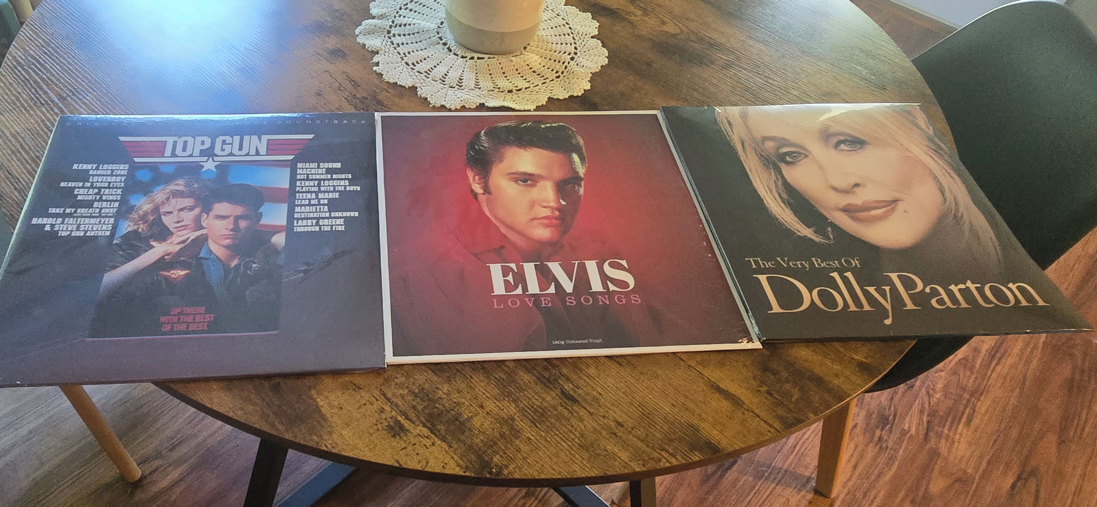 Three vinyl records on a round wooden table.