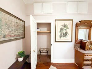 A hallway with a door leading to a closet, a framed botanical print, a small potted plant, and a mirror on a dresser.