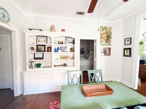 Un comedor con una mesa verde, muebles blancos con estantes y vista a un dormitorio.