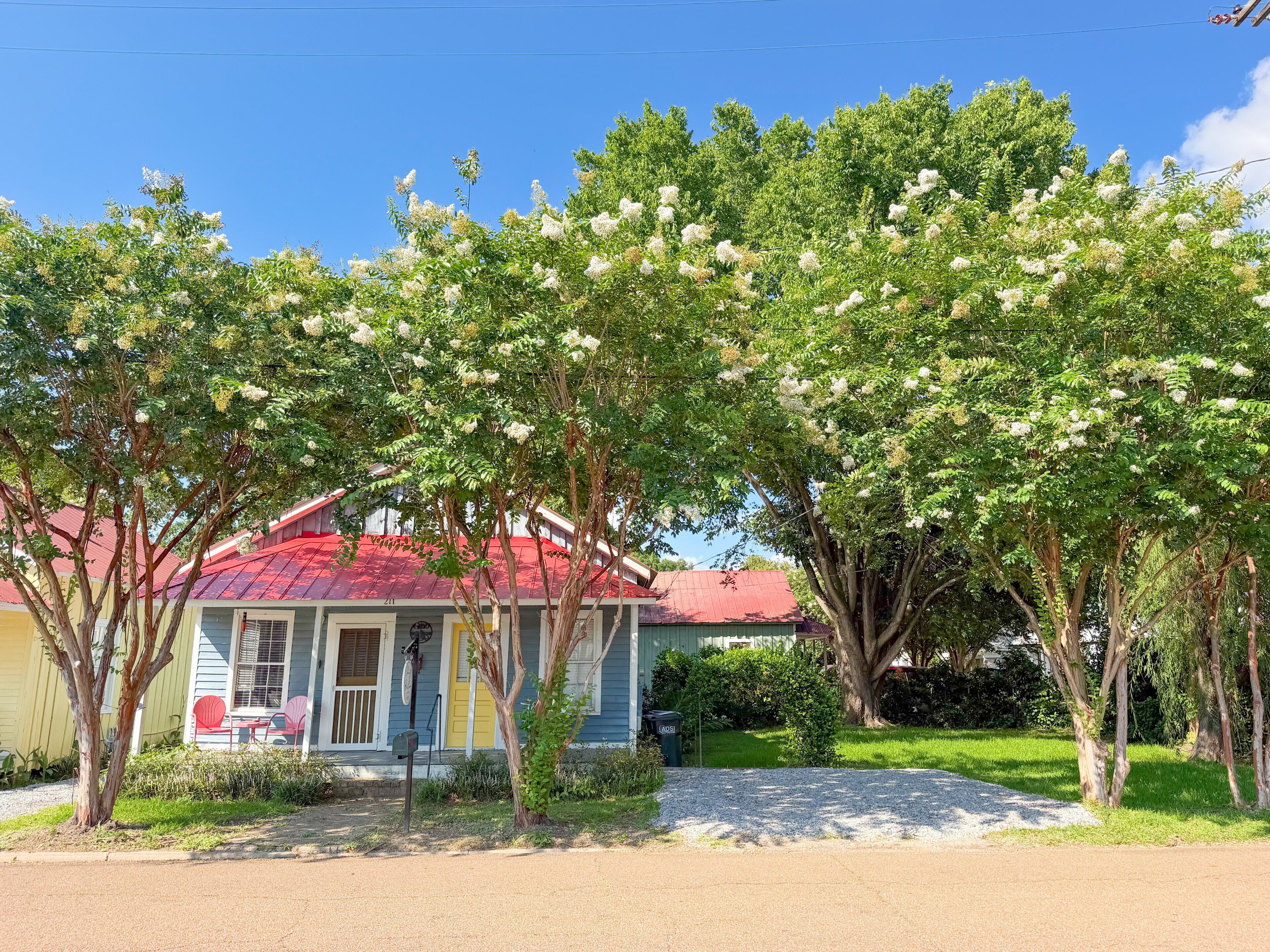 A house with a red roof, surrounded by trees with white flowers, and a clear blue sky.