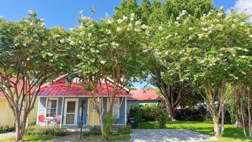 A house with a red roof, surrounded by trees with white flowers, and a clear blue sky.