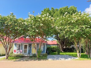A house with a red roof, surrounded by trees with white flowers, and a clear blue sky.