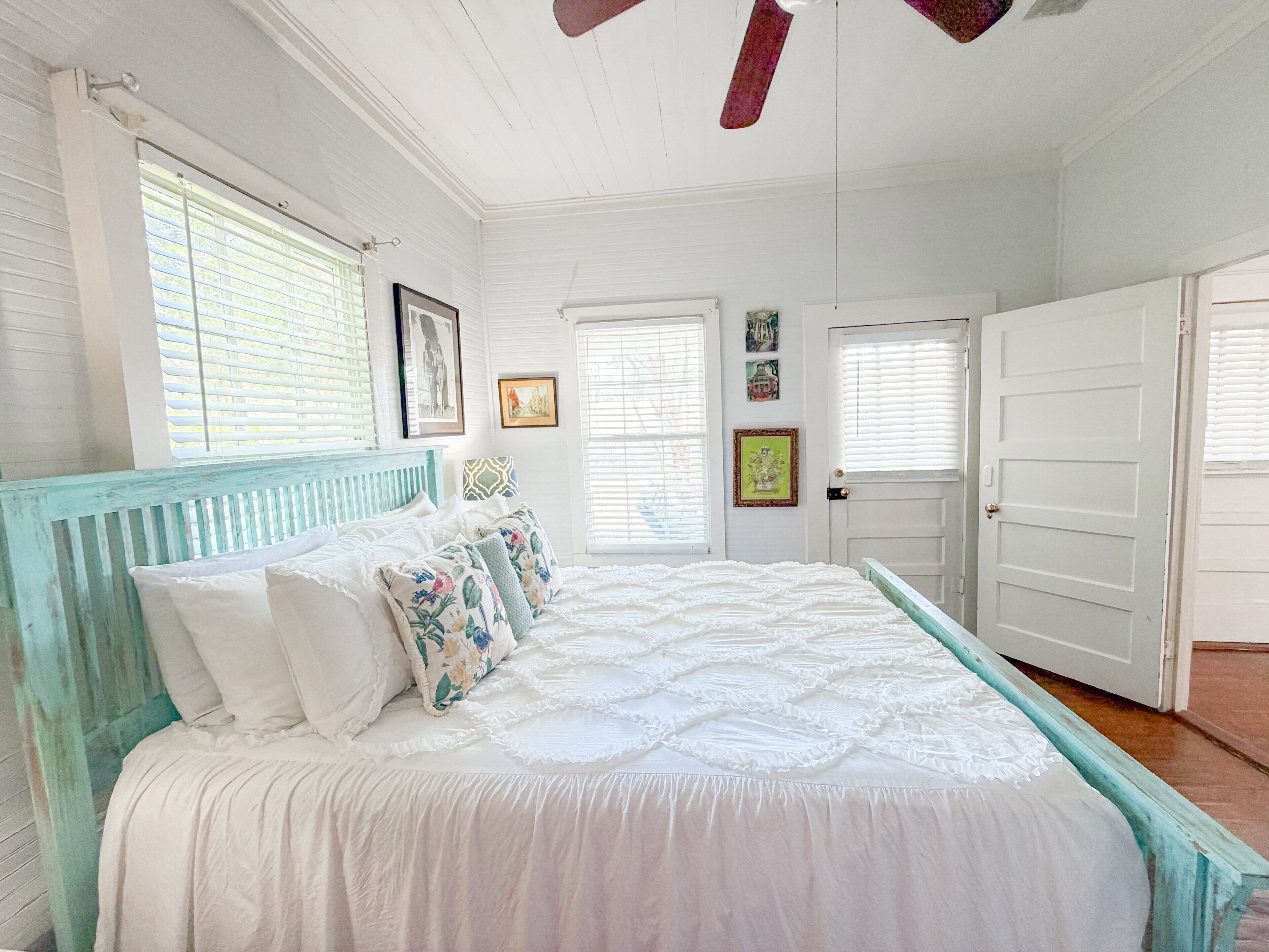 A bedroom with a bed, white walls, a ceiling fan, and a door.